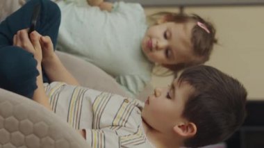 Çocuklar, kız ve erkek kardeşler telefonda oynuyorlar sandalyede oturuyorlar, evde dinleniyorlar. Eğitim, okuma konsepti. Modern cep telefonu teknolojisi kavramı