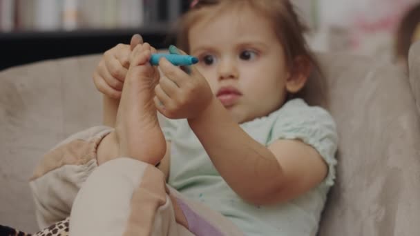 青いマーカーで遊んでいる小さな子供の赤ちゃんの女の子は 自宅でソファでリラックスしています かわいい女の子の絵 青絵具 — ストック動画