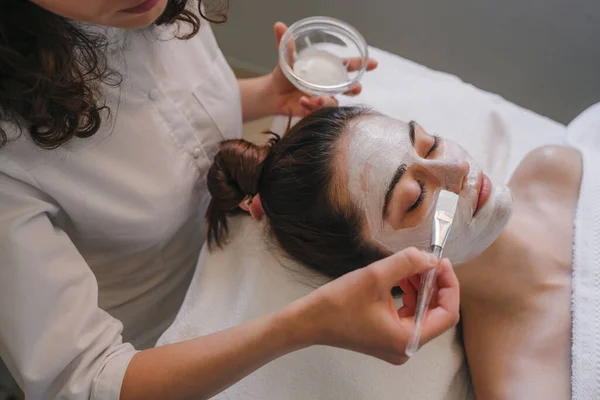 美容师把面霜涂在年轻女性的额头上 涂在温泉沙龙 皮肤治疗 女童面部治疗 — 图库照片