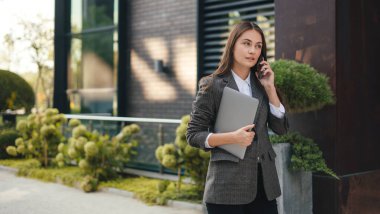 Şehirde bireysel stil ve moda sergileyen mutlu genç bir kadın. Telefonda konuşmak ve elinde bir dizüstü bilgisayarla....