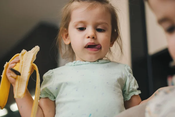 Menina Comendo Uma Banana Enquanto Olha Para Irmão Casa Foto — Fotografia de Stock