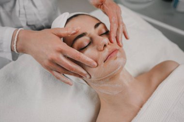 Evdeki aydınlık yatak odasında yatarken yüzüne krem süren isimsiz bir kadının en iyi görüntüsü.