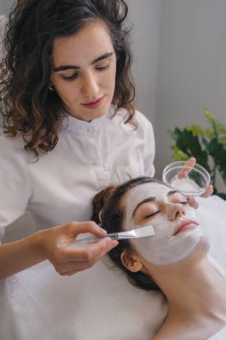 Evde cilt bakımı rutini sırasında aydınlık odada maske takan genç bir kadın.