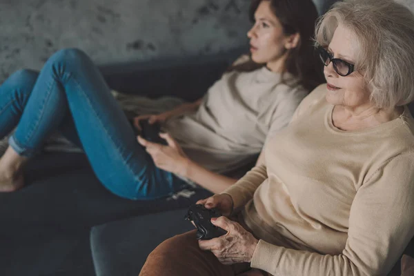 stock image Side view of young couple in casual clothes sitting on sofa and playing video game while spending time together in living room