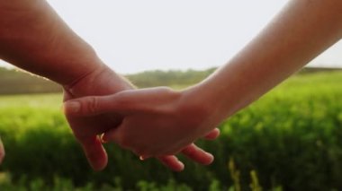 Gün batımına karşı bulanık yeşil bir alanda tutunan bir adam ve kadının eli. Çift gol. Özgürlük.