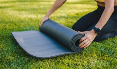 Parkta yoga yaparken hasıraltı edilmiş spor kıyafetli, mindere oturmuş bacaklarını esneten anonim kadın sporcu yan görüntüsü