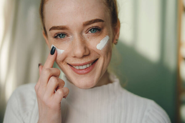 Позитивная молодая женщина с повязками на глазах, улыбающаяся и смотрящая в камеру, стоя в светлом помещении