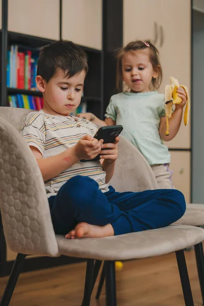 귀여운 소년은 집에서 방에서 시간을 보내면서 의자에 앉아서 스마트폰으로 비디오 — 스톡 사진