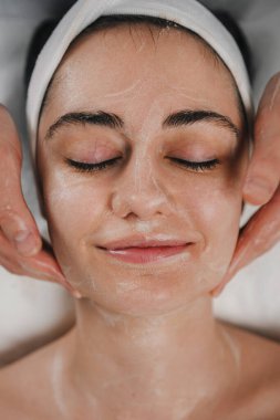 Kapalı gözlü, kaplıca salonunda yüz masajı yaptıran güzel bir kadının yakın portresi..