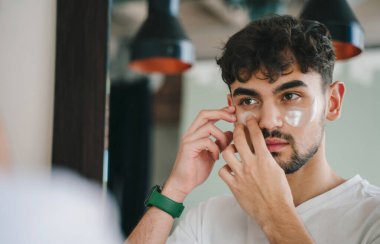 Genç sakallı bir erkek sabahları aynaya bakarken yamalar yapıştırıyor..