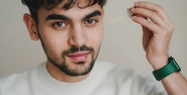 Porträtt Söt Ung Man Som Applicerar Genomskinligt Serum Ansiktet Medan — Stockfoto