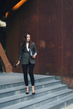 Kendine güveni tam, modaya uygun giyinmiş genç bir kadın merdivenlerde kameraya bakıyor.