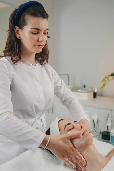 美容师用泡沫洗净一位女性病人的面部皮肤 女人的皮肤护理程序 天然化妆品面部整容治疗 — 图库照片