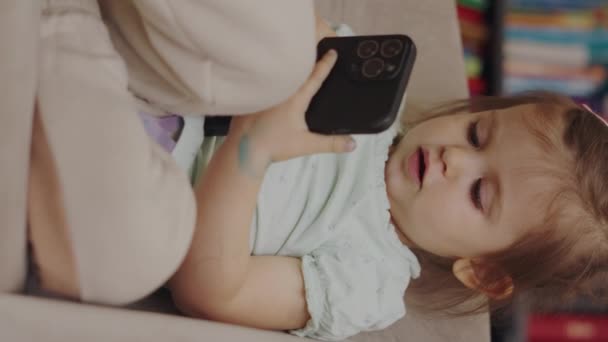 ソファーに座っている赤ちゃんは スマートフォン画面に触れ ソファーでゲームをすることに深く魅了されました 約2歳の子供 — ストック動画