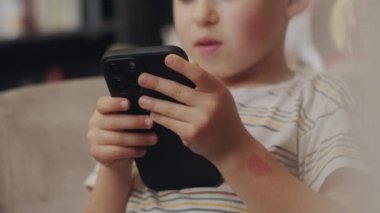 Cep telefonuyla oynayan, video izleyen, oturma odasındaki koltukta oturan mutlu küçük çocuk. Bağımlılık. Eğlence ve eğlence uygulaması.