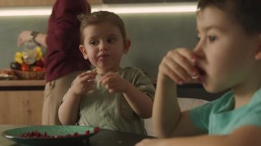Mutfak masasında oturan tatlı, neşeli erkek ve kız bebek bir tabak dolusu sulu, kırmızı, taze nar çekirdeği. Sağlıklı beslenme. Yaşam biçimi