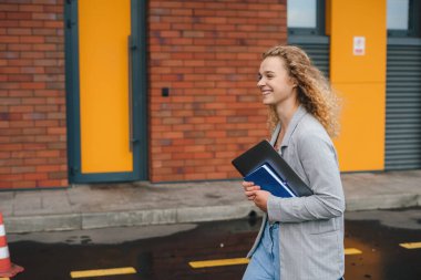 Bilgisayarlı bir kız öğrencinin kampüsün girişine ya da üniversitesinin fakültesine gidişinin yan görüntüsü. Eğitim kavramı.