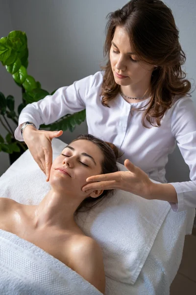 Professional therapist making skin lift procedure to relaxed mature female lying on table in spa salon. Relaxing treatment in medicine