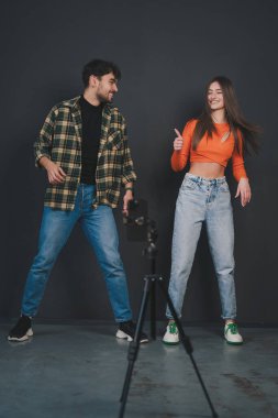 Sosyal medya için günlük kıyafetlerle dans eden güzel bir çift viral video kaydediyor. Siyah arka planda izole edilmiş. Mobil cihaz kullanılıyor. Günlük konsepti