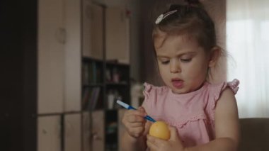 Mutfakta vakit geçirirken elinde yumurta tutan ve üzerine keçeli kalemle çizen mutlu bir kız çocuğu. Mutlu Paskalyalar.