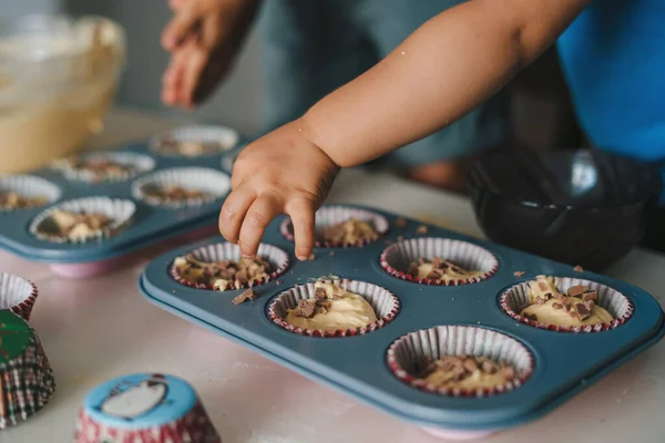 stock image Little babys hand sprinkling Chocolate on ripe cupcakes. Family having fun cooking muffins. Adorable child helping.