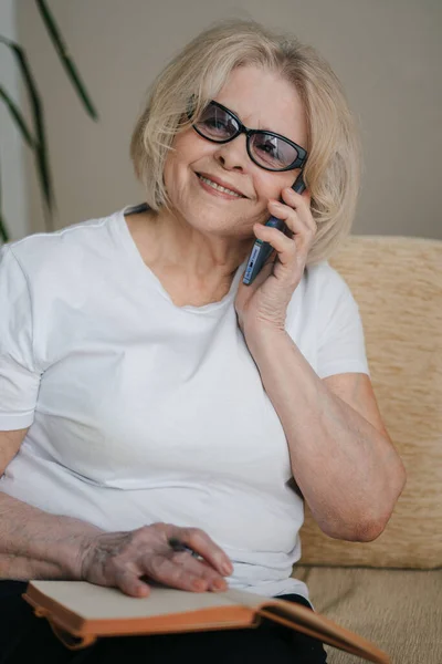 Senior businesswoman on a phone call writing on her planner at home.
