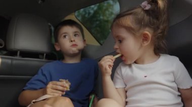 İki çocuk açık bagajda oturup abur cubur yiyorlar, arayı kapatmak için geziye ara veriyorlar. Aile otomobil tatili. Yolculuk.