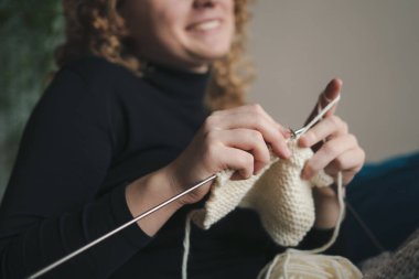 Kadınların ellerinin iplikten örgü iğneleriyle ördüğü yakın çekim görüntüsü. Evde örgü örme kavramı. Konforlu ev ve stres karşıtı hobi.