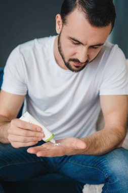 Beyaz yetişkin bir adam tüpten nemlendirici krem sürüyor. Erkek yüz bakımı ve eşleştirme konsepti