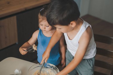 Mutfakta yemek pişirirken kasede malzemeleri çırpan sevimli çocuklar. Tatil için aile tarifleri.