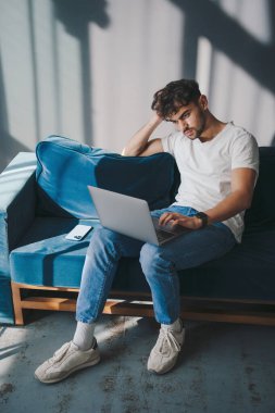 Evdeki kanepede oturup bilgisayar klavyesinde yazarak uzaktan çalışmaktan zevk alan yakışıklı bir adam. Kanepede dinlenen neşeli, sıradan bir erkek. Eğleniyorum.