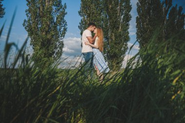 Yeşil çim tarlasının ortasında öpüşen romantik bir çiftin çok uzak bir görüntüsü. Birlikte sakin bir alanda.