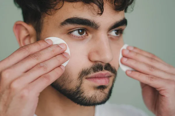 Males daily skincare routine with toner and cotton pads cleaning face skin isolated over studio background. Refreshing rejuvenation. Skin care healthcare