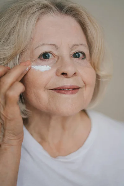 stock image Close-op of positive caucasian senior woman using day moisturizer, anti-aging cosmetic cream to hide wrinkles, doing a daily beauty routine. Cosmetology.