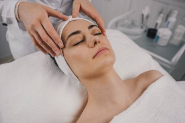 Kafkasyalı hoş bir kadın güzellik salonunda vakit geçiriyor. Yenilenme fırçası. Yüz dermatolojisi maskesi. Detoks terapisi
