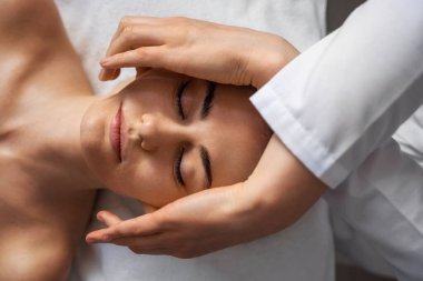 Güzellik kliniğindeki kadın hastaya yüz gerdirme masajı yapan cildiyecilerin ellerine yakından bakın. Kozmetoloji kavramı.