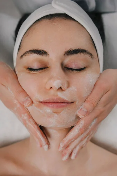 Cosmetologists hands cleansing the skin with foam. A womans skin care procedure. Natural cosmetics. A beautiful face. Cosmetic treatment of the face