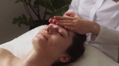 Kanepede yatan genç bayan müşterinin yüzüne masaj yapan profesyonel bir güzellik uzmanı. Spa tedavisi konsepti. Vücut masajı. Güzellik salonu.