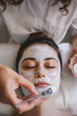 Kaplıcadaki güzellik salonunda beyaz maske takan genç ve güzel bir kadın. Yüz bakımı. Kozmetik işlem.