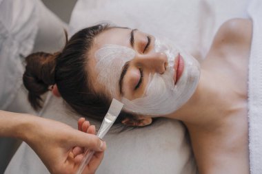Genç bir kadın spa salonundaki partiküllerle besleyici yüz maskesi alıyor. Güzel bir kadın cilt bakımına gider. Yüz bakımı. Kozmetik prosedürü. Sağlıklı yaşam tarzı