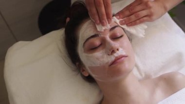 Güzellik uzmanlarının elleri maskenin yüzünü mendille temizliyor. Profesyonel güzellik salonu. Kız yüz tedavisi. Kozmetik prosedürü. Güzellik