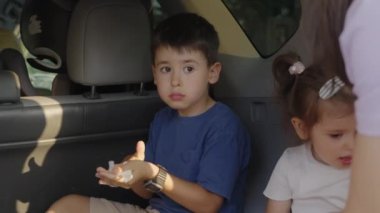 Çocuklar arabanın bagajında otururken abur cubur yiyorlar. Yemek konsepti. Mutlu aile, yaz, tatil. Macera yolculuğu.