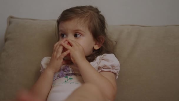 ハッピーな赤ん坊の女の子は 赤いリンゴを食べるソファーに家に座っています 高品質のビデオ — ストック動画