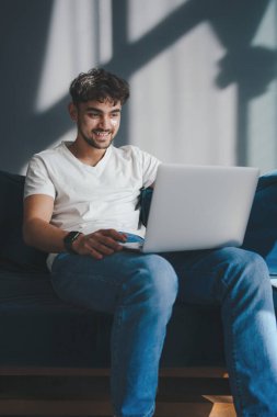 Adam kanepede dinleniyor, hafta sonunun tadını çıkarıyor. Rahat koltukta oturarak rahatla. Modern iç mekan. İnternet teknolojisi. Laptop kullanılıyor.