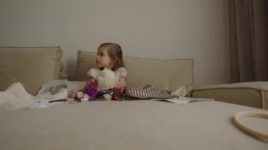 Şirin küçük kız evdeki kanepede oturmuş örgü ipliklerle oynuyor..