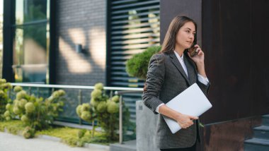 İş kadını ara veriyor ve elinde dizüstü bilgisayarla cep telefonuna cevap veriyor. Konsept: iş, girişimci, yönetimsel. Boşluğu kopyala.