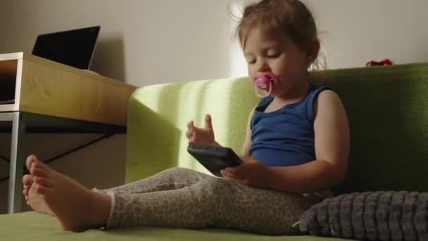 ポータブルゲームコンソールの画面を見ている赤ちゃんの少女は 部屋のソファーに座っています ビデオゲーム モバイルゲーム バーチャルリアリティ Eスポーツ — ストック動画