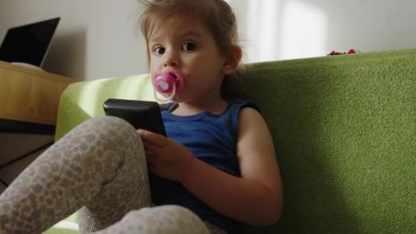 可爱的高加索女婴在玩电子游戏时吸吮奶嘴 电脑娱乐 — 图库视频影像