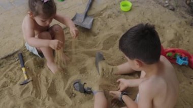 Mutlu küçük çocuklar: erkek ve kız dışarıda, kır bahçesinde oyun sahasında kum oynamaktan zevk alıyorlar. Çocuk parkı. Kum oyunu. Yazın açık hava eğlencesi.