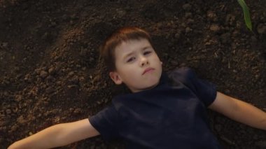 Kahverengi saçlı neşeli bir çocuk ve bahçede yerde yatan siyah tişörtlü bir çocuk manzarası. Sağlıklı yaşam tarzı - doğadaki çocuklar ve